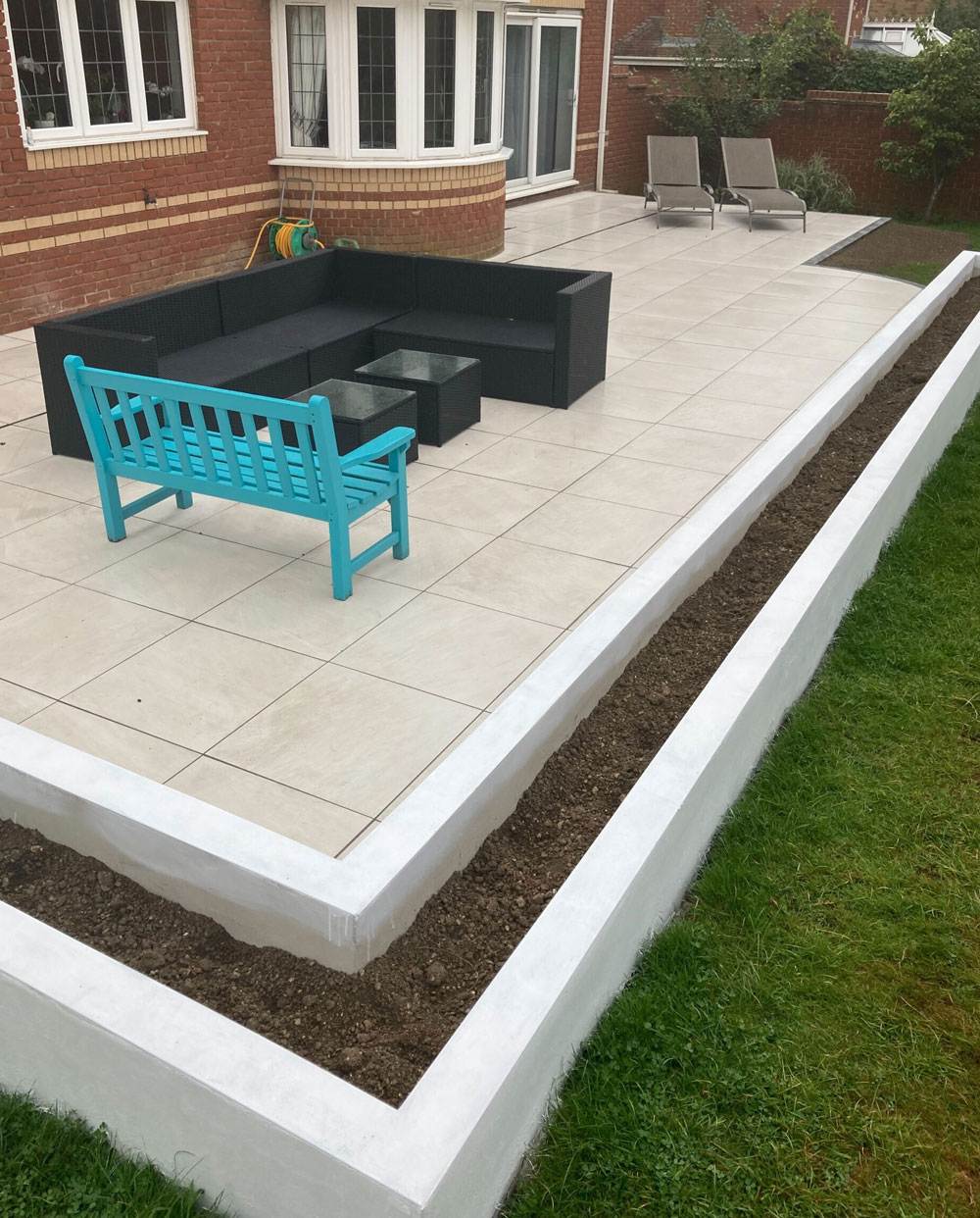 Image shows a newly laid patio with raised beds around the edge and garden furniture on top. Image depicts Thomas Charles Landscapes' professional garden landscaping