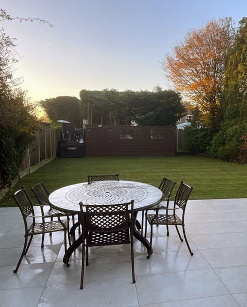 Image shows an outdoor table and chairs on a patio with a lawn beyond. Image depicts Thomas Charles Landscapes as expert garden landscapers