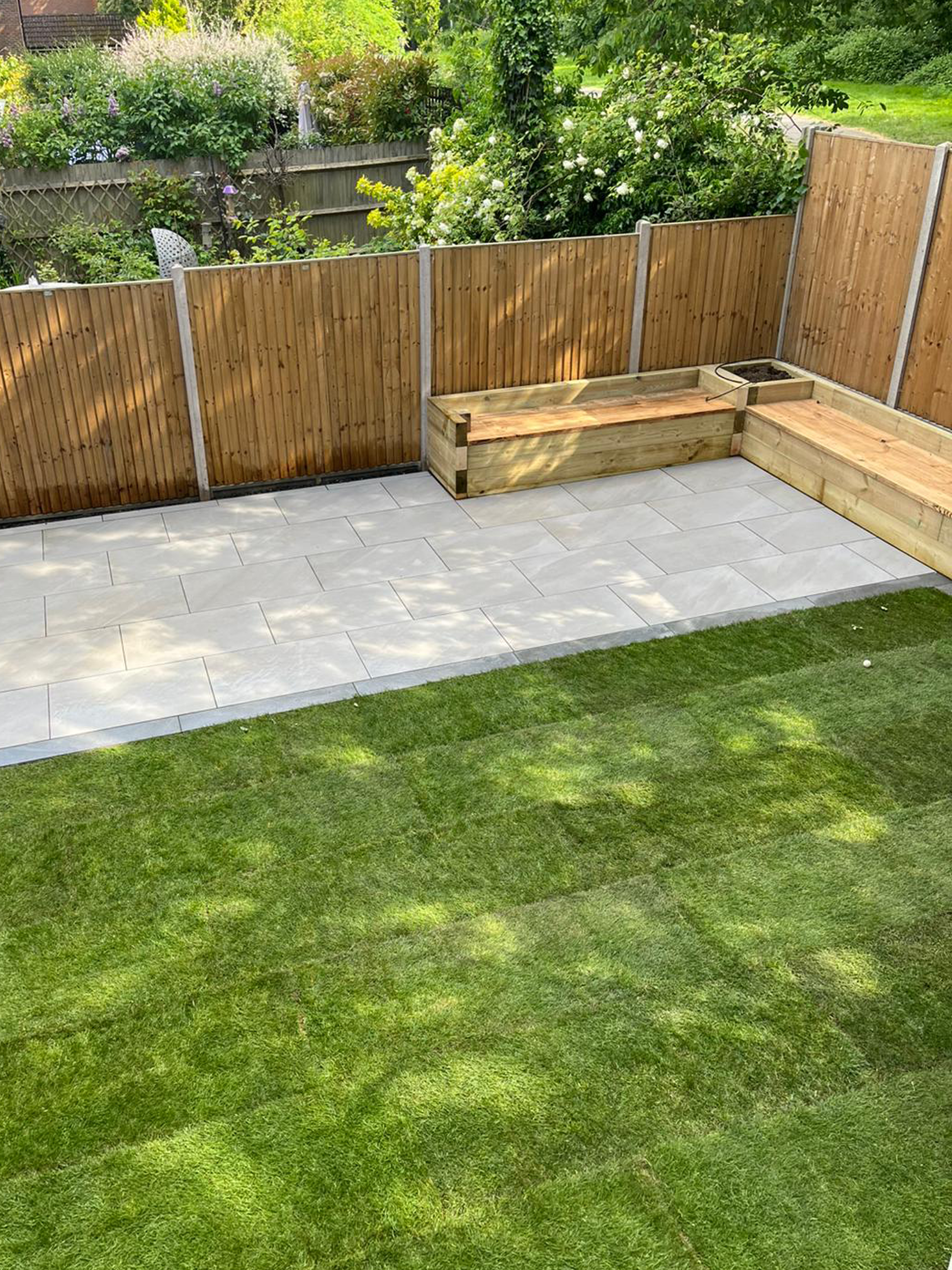 Image shows newly laid turf and patio with built in seating sear and planters. Image depicts Thomas Charles Landscapes' garden landscaping expertise